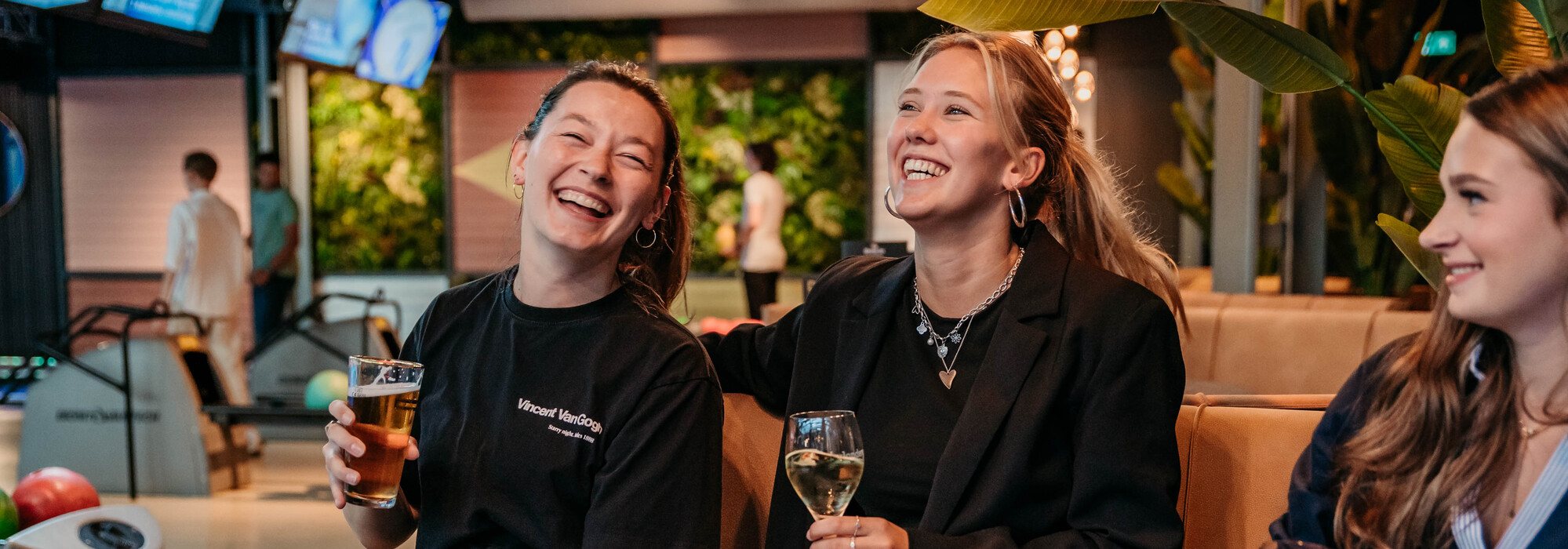 Drie vrouwen zitten aan tafel met drankjes bij Mitland Bowling