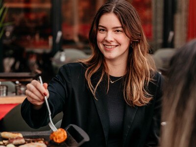 Woman placing a piece of meat on the table grill with a fork